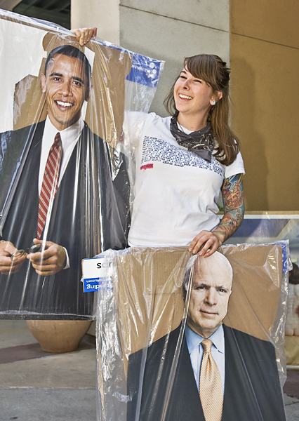 Smiling woman holds up cardboard cut-outs of Barack Obama and John McCain.