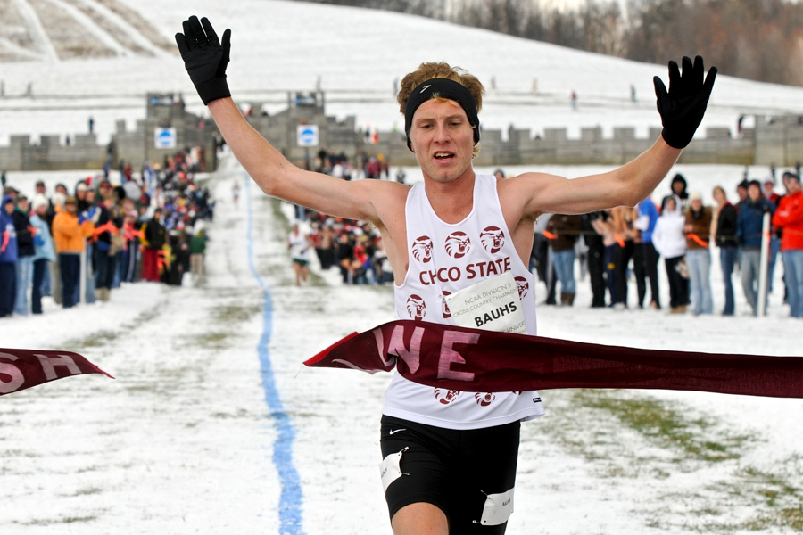 Chico State runner crosses finish line with arms spread out; snow-covered hill in background.