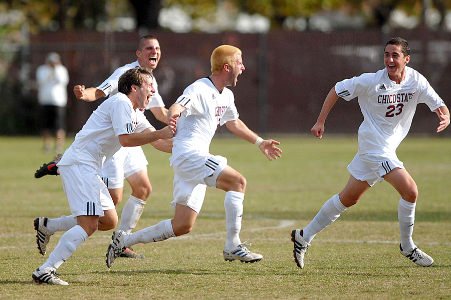 Four Chico State athletes run from left to right in celebration; one holds the hero's jersey.