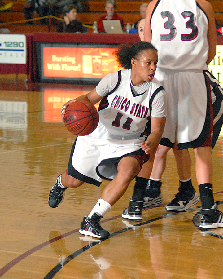 Chico State basketball player drives left to right around screener, ball in her right hand.
