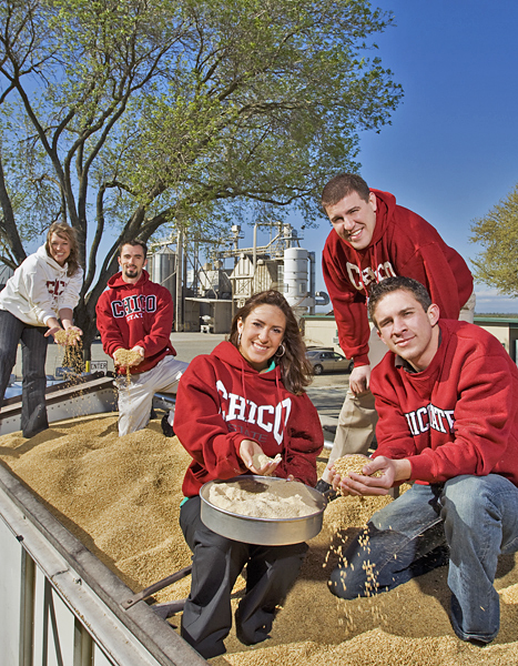 Three men and two women, all wearing Chico State sweatshirts, stand in an almond delivery truck holding the product and smiling.