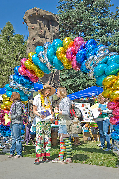 Women in colorful leg-wear converse beneath mylar-balloon arch; climbing tower looms in back.