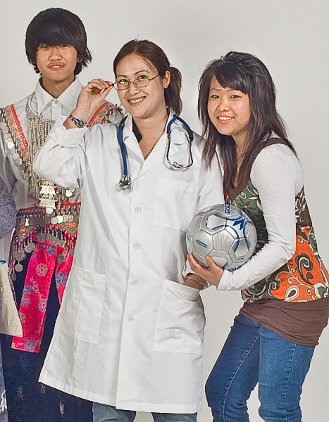 International students smile; man in cultural clothing, woman in lab coat, woman holds ball.