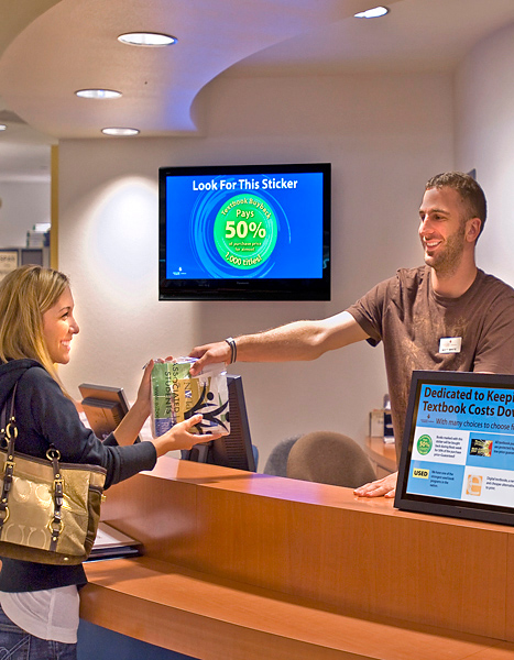 blng07_Female (left) accepts newly purchased books from male cashier (right) with arm extended.