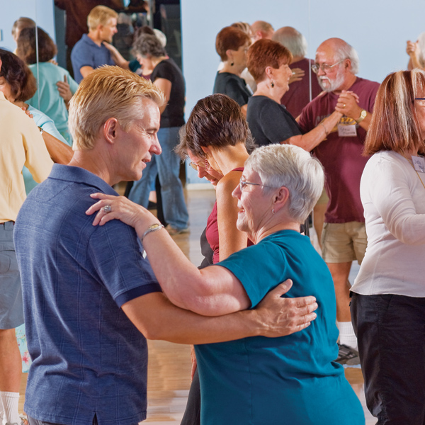 Couple in a dance class face each other and embrace in slow dance posture smiling.