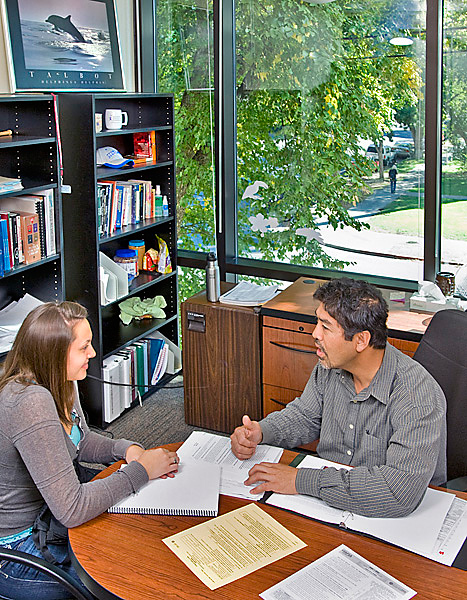 Two people seated across a desk discuss financial aid. Woman on left, man on right. 