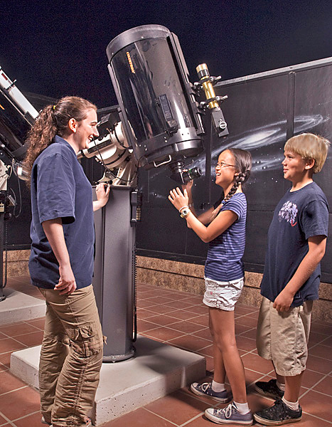 Woman assists two children with a powerful telescope in the planetarium. 