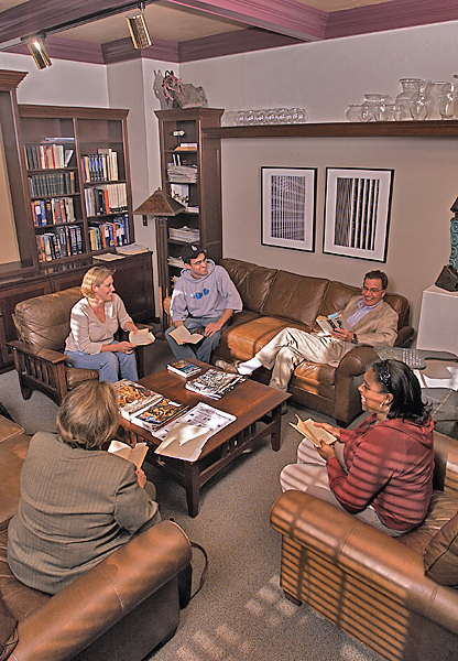 Five people sit on leather couches and chairs in a well-kept study or office discussing a book that all hold.