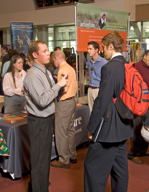 Man (left) lists points using hands for man with back pack (right) during Career Fair.
