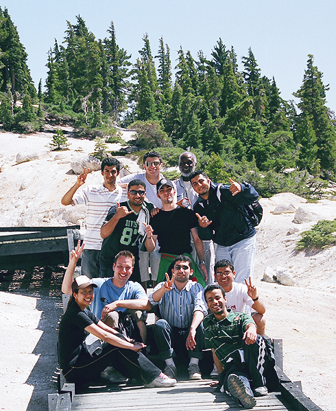 A group of exchange students pause their hike to pose in two groups. One group sits on a wooden path and the other stands being them. Members of both groups hold up two-fingered peace signs.