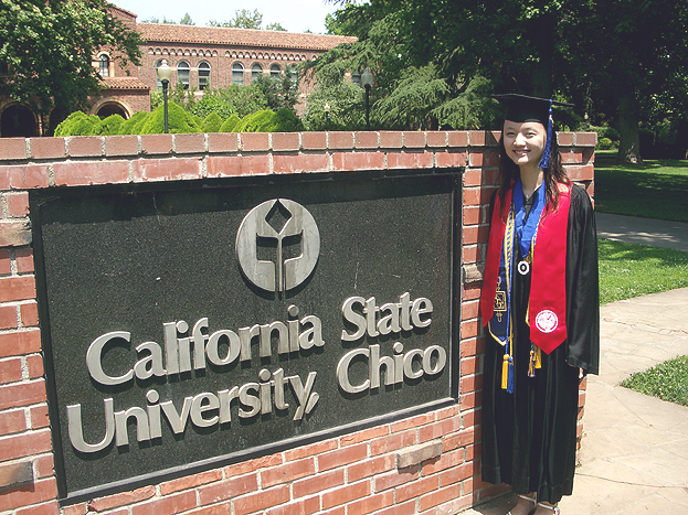 Female international graduate poses next to the California State University, Chico sign with Kendall Hall in the background.