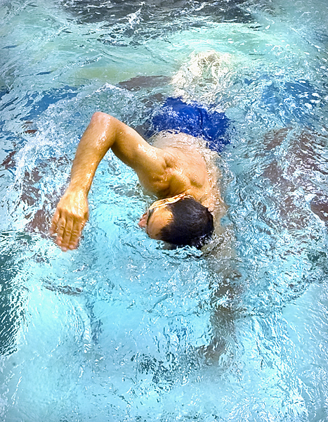Man in blue swim trunks is in mid-swim stroke moving towards camera.