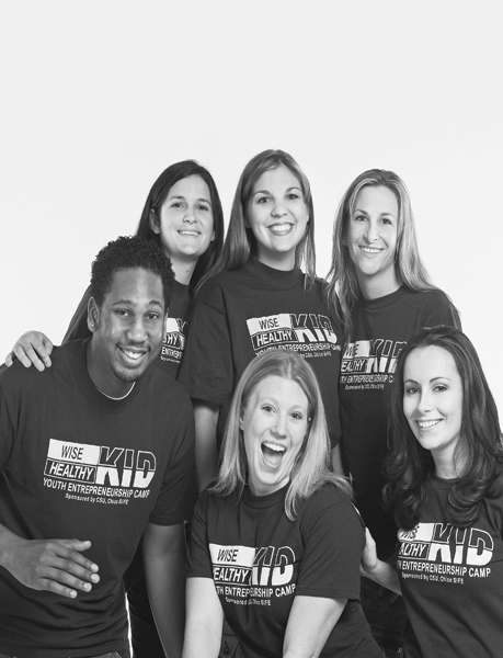 Three women stand behind two women and man kneeling all wearing Wise Kid, Health Kid t- shirts.