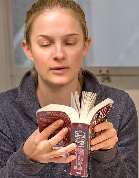 Woman in grey sweater flips through an Oxford dictionary and thesaurus that she is holding.