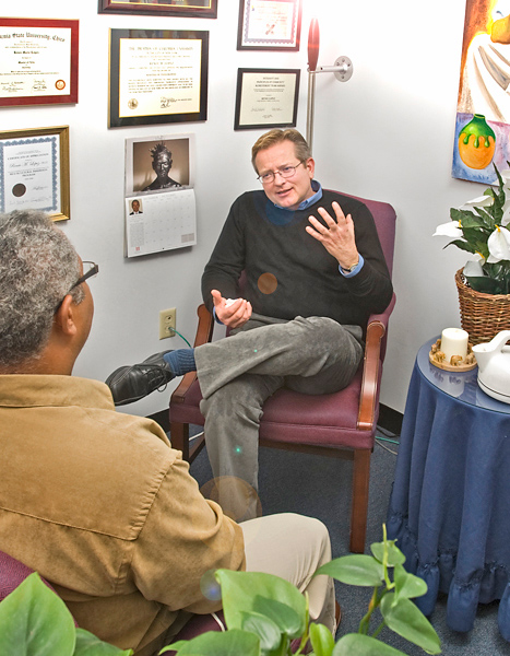 Over shoulder look in at a counseling session; one man gestures while talking to another man who's back is to the camera.