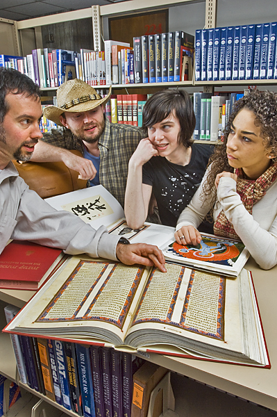 Man points to a passage in a Celtic religious book, while two women and another man compare three other books of cultural religious images from Japan and India.