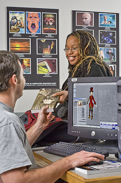 Man sitting at a computer is given a book by a smiling woman wearing glasses.