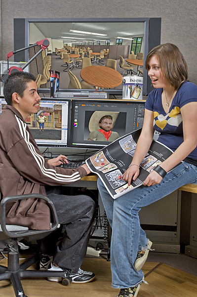 Man and woman sit at a digital design studio workstation. She holds and points to a frame in a storyboard.