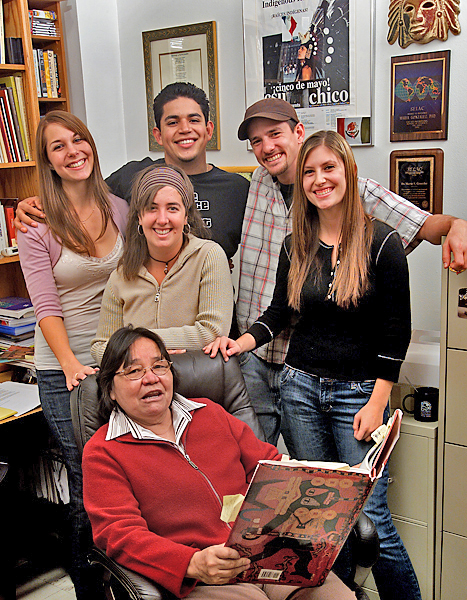 Five students smile and huddle around a woman holding a really big book.