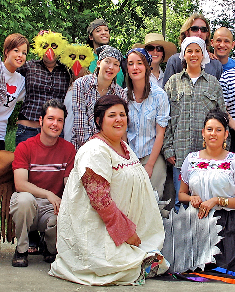 A diverse group of students huddle together with some dressed in traditional cultural clothing and two others wearing chicken masks.