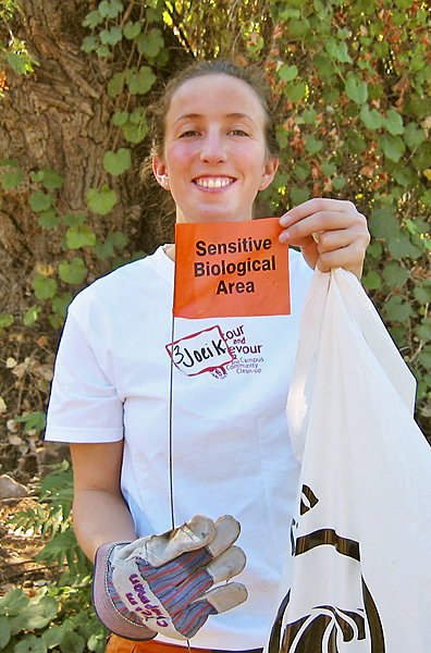 Woman holds up an orange "Sensitive Biological Area" flag and smiles.