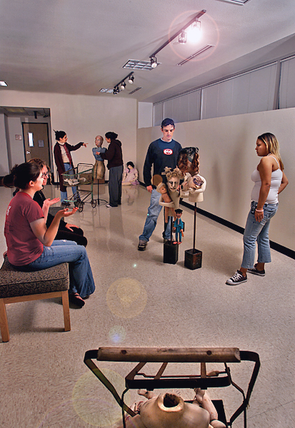 People stand around and look at art sculptures. Two people sit on a bench.