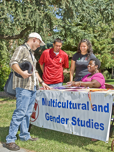 One man holding a bike helmet stops at a MCGS information table where a department advisor and two other representatives from student organizations smile and pass out printed information.