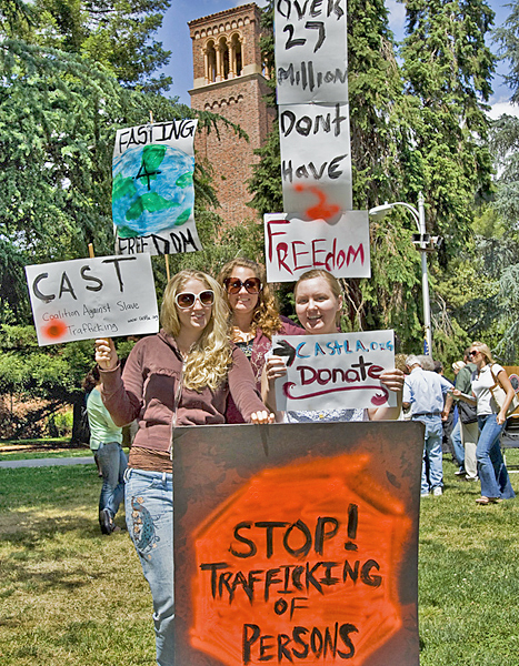 Three women, two of whom wear sunglasses, hold signs protesting human trafficking. 