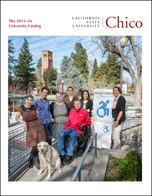 Seven individuals huddle together outside around a vertical white banner of the new accessibility icon, adopted by CSU, Chico in 2014.  The group of four women and three men smile while facing the viewer.  They stand under a blue sky with striated clouds cascading off into the distance and the Trinity Hall bell tower rises behind them.
