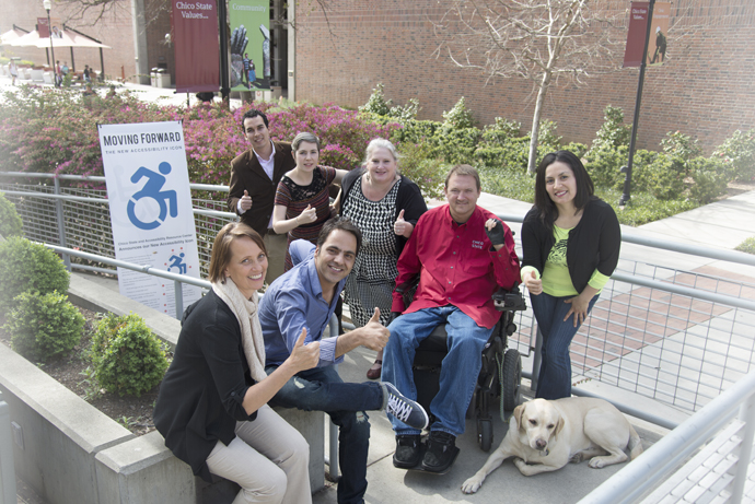 SEven people and a dog pose outside next to a vertical banner of the new accessibility icon, with the words 