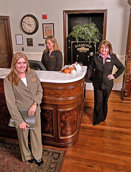 Three women stand around the front desk of a hotel lobby dressed in business attire.