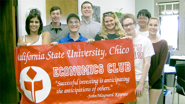 Eight students hold up a banner for the Economics Club on the CSU, Chico campus.  They stand indoors and smile at the camera.