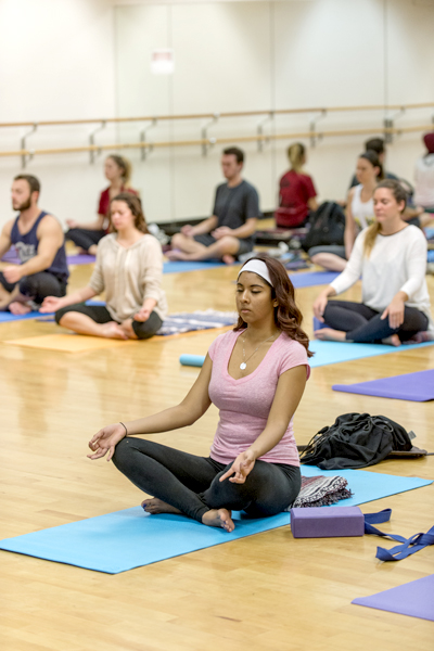 Female student is captured sitting in the basic seated pose with multiple students behind her all in the same basic seated pose.  