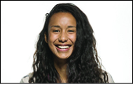 Woman with long wavy, brown hair smiles in front of a white background.  