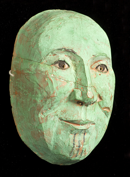 A crude looking green human mask against a black background.