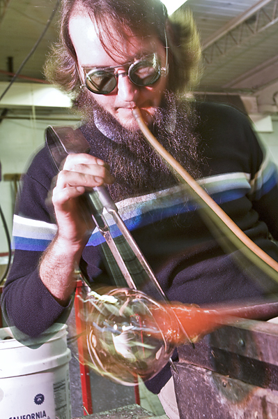 Man wearing protective goggles blows glass.