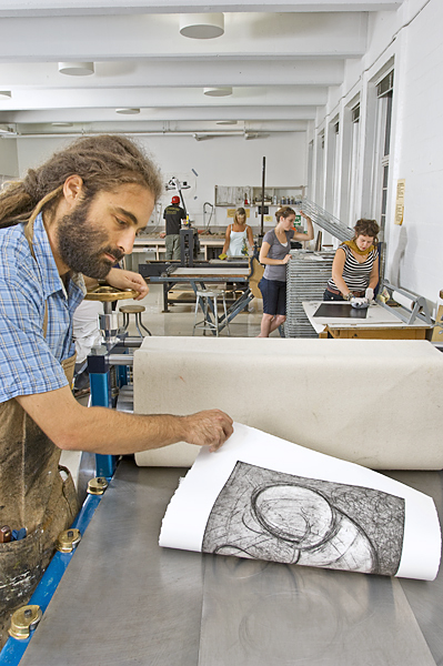 Man inspects a print following a pass through the printmaking press.