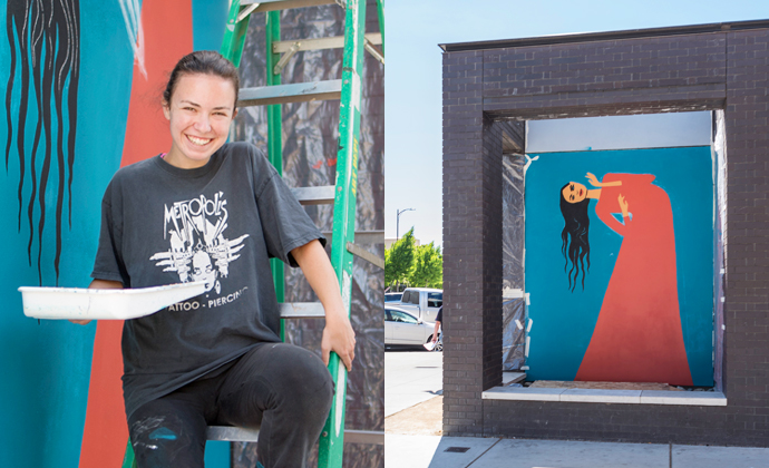 Female student sits on ladder holding a paint tray.  Behind and to the right of the student is a mural of woman bending at waist.