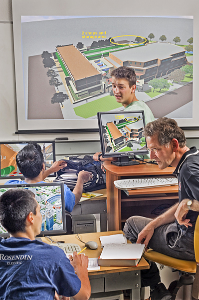 Four men sitting in a computer lab with a computer-generated 3D model of several structures on the monitors of each computer as well as on a pull-down screen behind them.