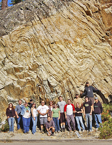 A little over a dozen students stand in front of a rock formation illuminating a fingerprint-like pattern.