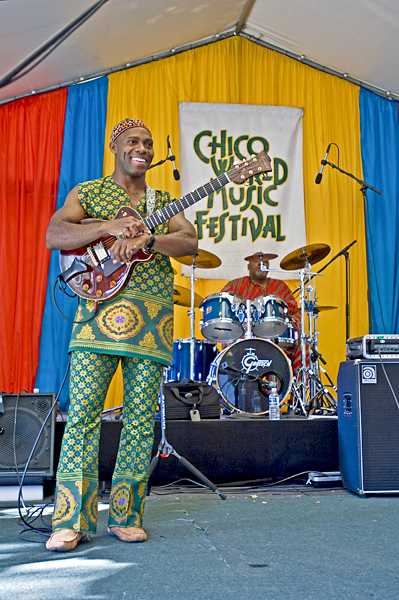 Performer at the annual Chico World Music Festival, stands with guitar. Drummer waits to begin behind him.