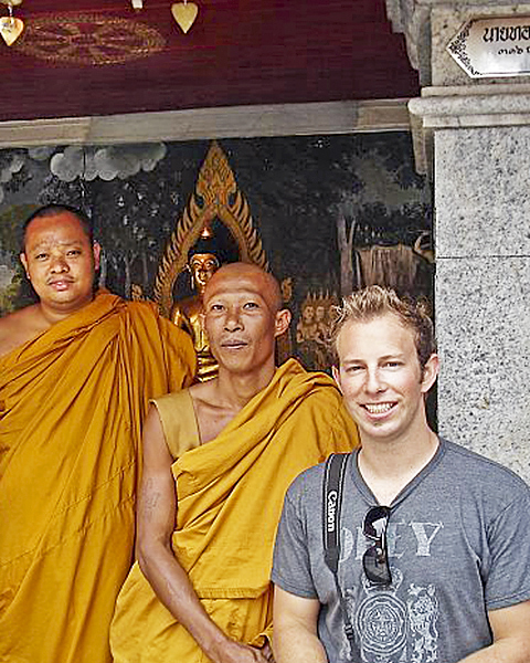 College-aged male stands with two Tibetan monks near an alter.