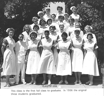 A group of women and one man stand on steps in a triangle (narrowing as it rises) in classic/vintage nurses outfits.