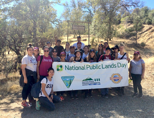 Several people gather in rows and pose for the photo.  A few individuals in front hold a white vinyl banner with the words "National Public Lands Day" printed in green letters on it.