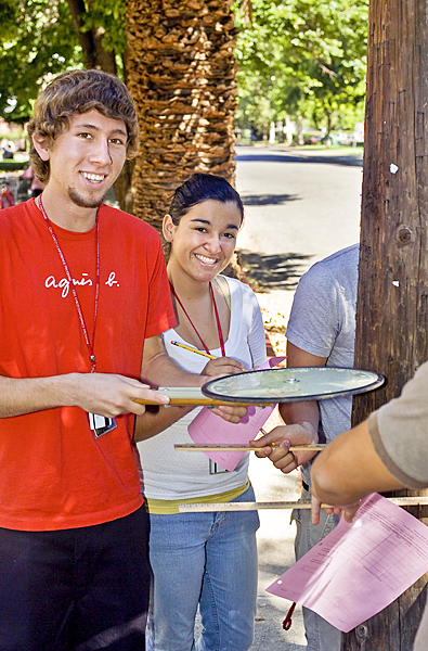 Man in red shirt holds a measuring wheel against a telephone pole in preparation to measure its circumference.