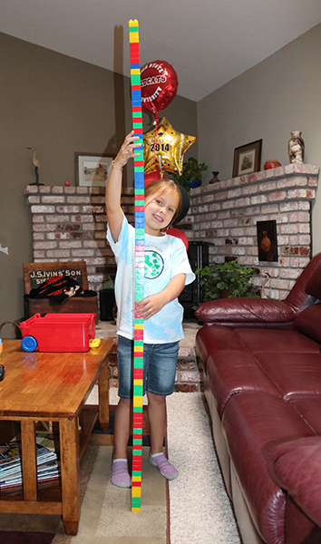 A young girl stands, without shoes, steadying a tower made of Duplo blocks.  The multi-colored tower is significantly taller than she.