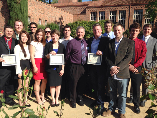 A group of both male and female students gather, smile, and pose behind Trinity Hall on the Chico State campus.  