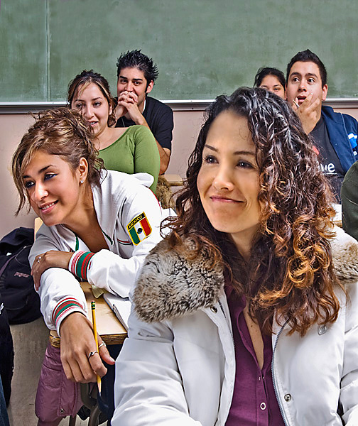 Classroom of students are captivated by unseen source. One guy in the back of the classroom stares at the camera.