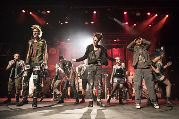 Three male dancers in front of other dancers on a stage with red soft lights.